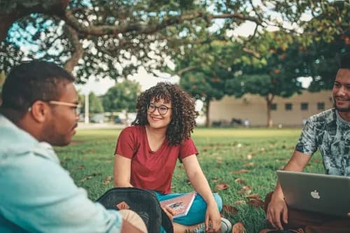 3 étudiants assis sur l'herbe et rigolant ensemble